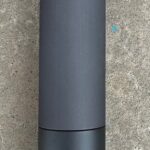 A black bottle sitting on top of a cement floor.