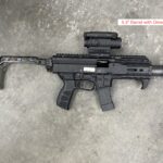 A black rifle with an extended barrel and a red dot sight.