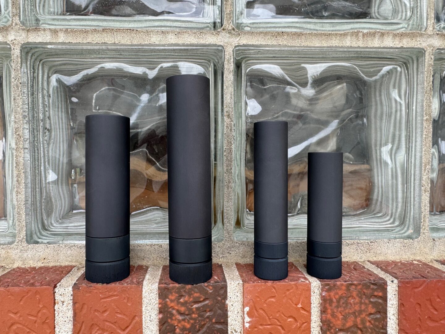 Four black cylinders are lined up on a brick wall.